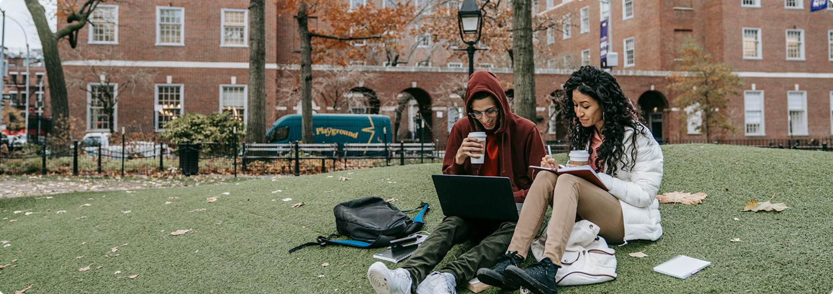 Two students drinking coffee and working together on the grass.